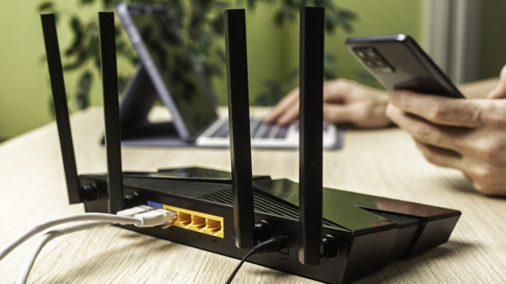 Perangkat router Wi-Fi hitam dengan antena eksternal dan kabel jaringan di atas meja kerja