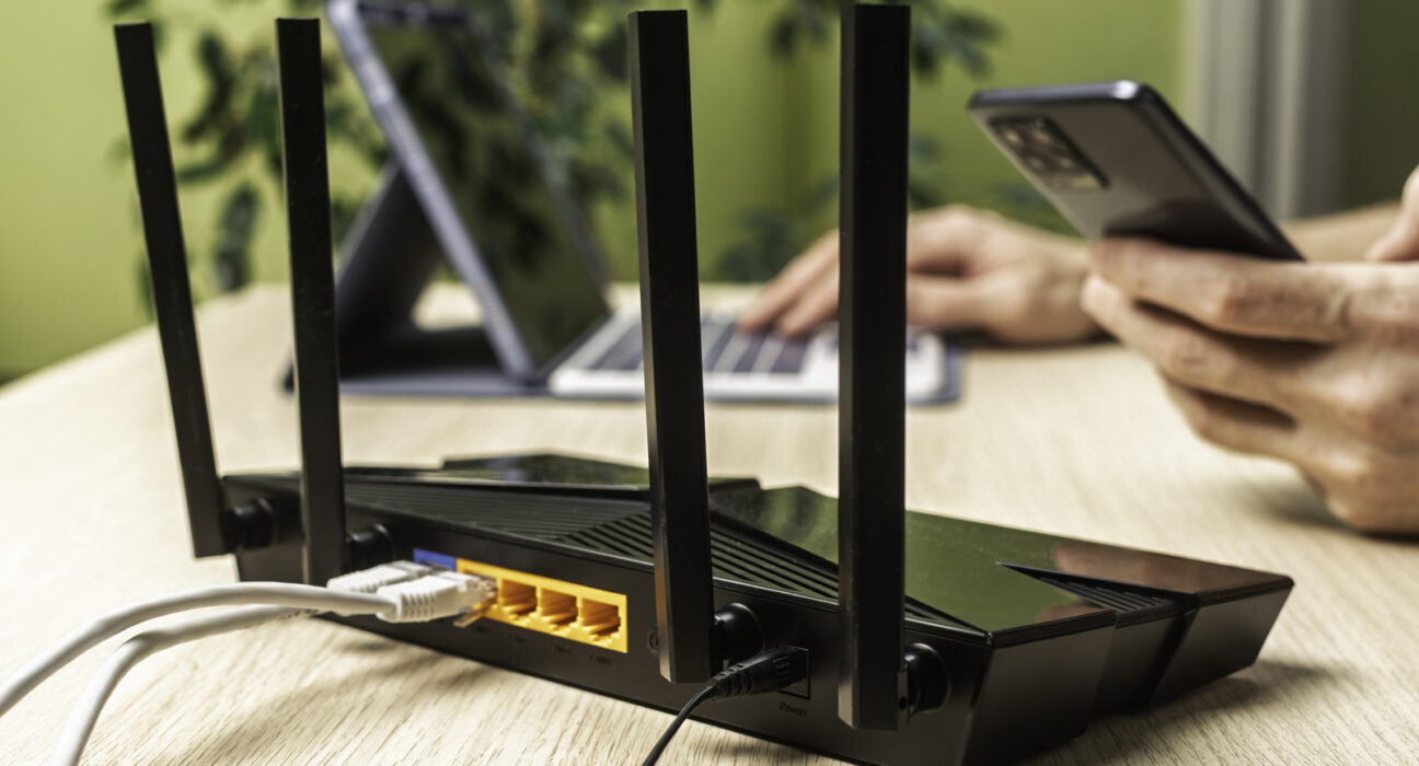 Perangkat router Wi-Fi hitam dengan antena eksternal dan kabel jaringan di atas meja kerja