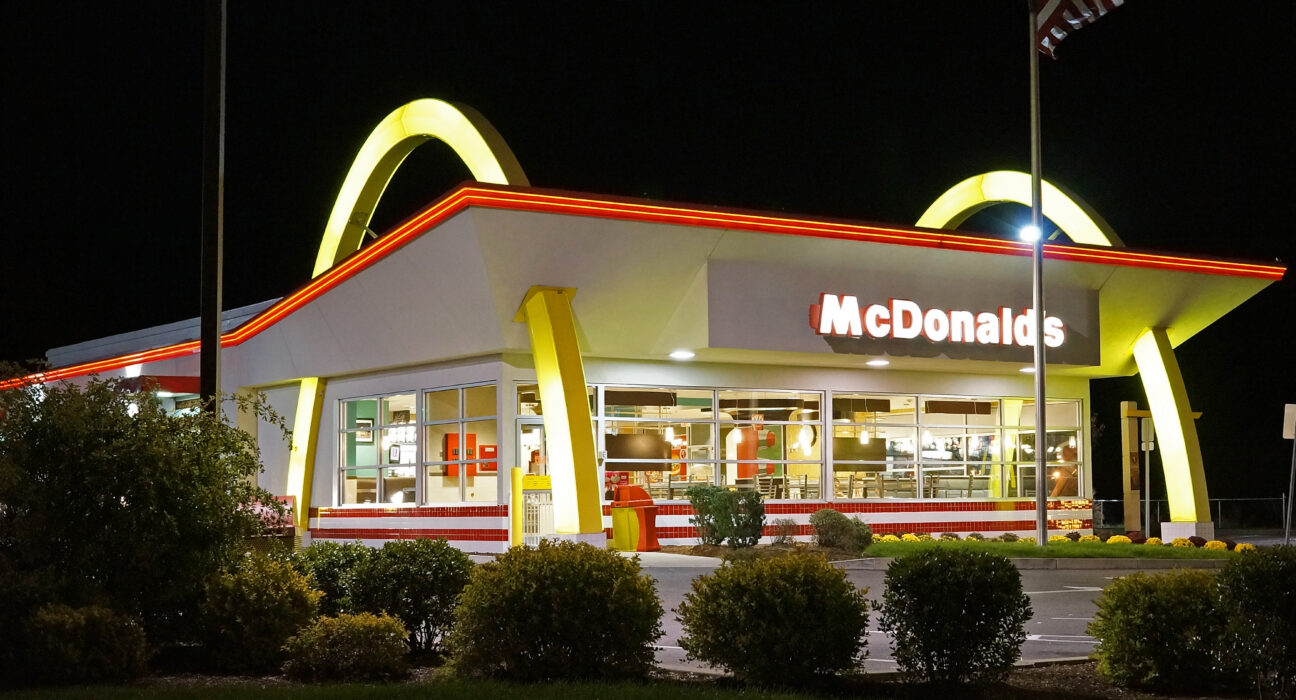 Papan logo Golden Arches restoran cepat saji McDonald's dengan latar langit cerah.
