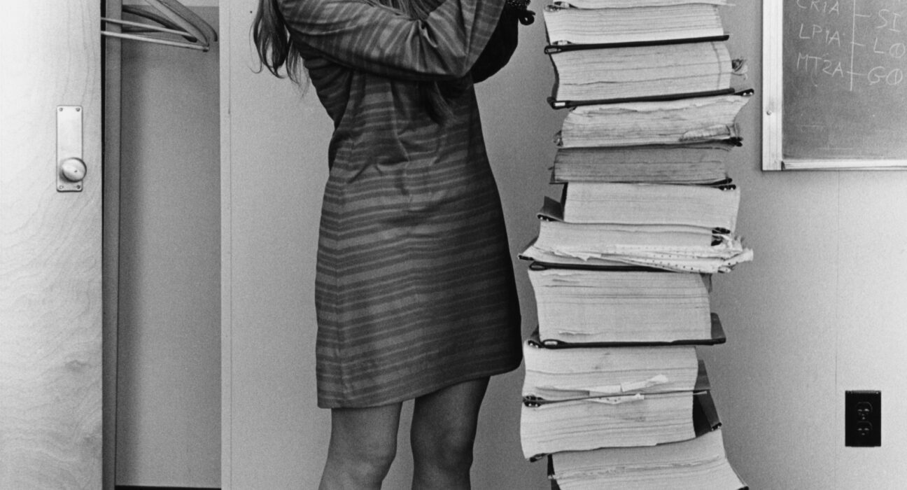Margaret Hamilton berdiri di samping cetakan kode program Apollo Guidance Computer pada 1969