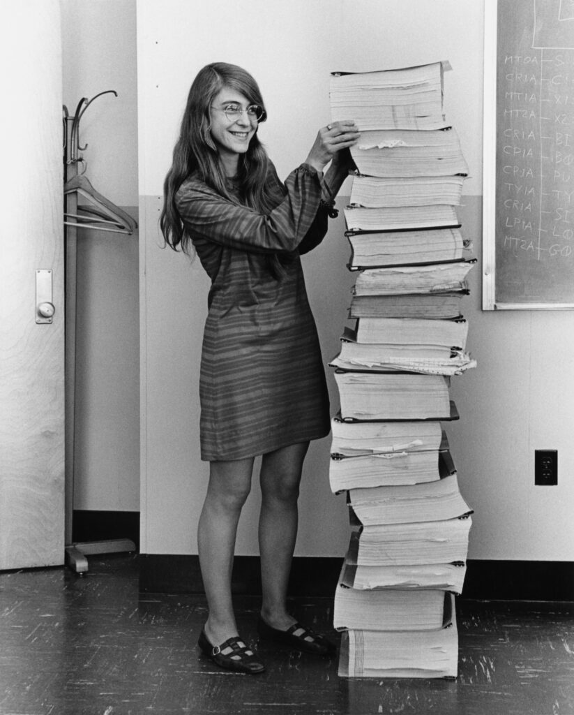 Margaret Hamilton berdiri di samping cetakan kode program Apollo Guidance Computer pada 1969
