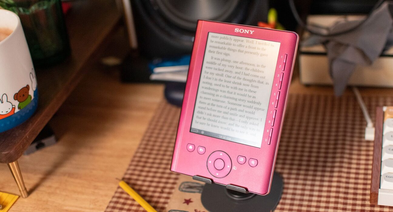 Perangkat e-reader klasik Sony Reader PRS-300 berwarna merah muda metalik di atas penyangga meja