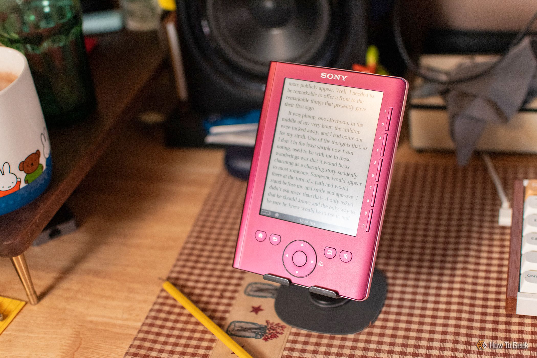 Perangkat e-reader klasik Sony Reader PRS-300 berwarna merah muda metalik di atas penyangga meja