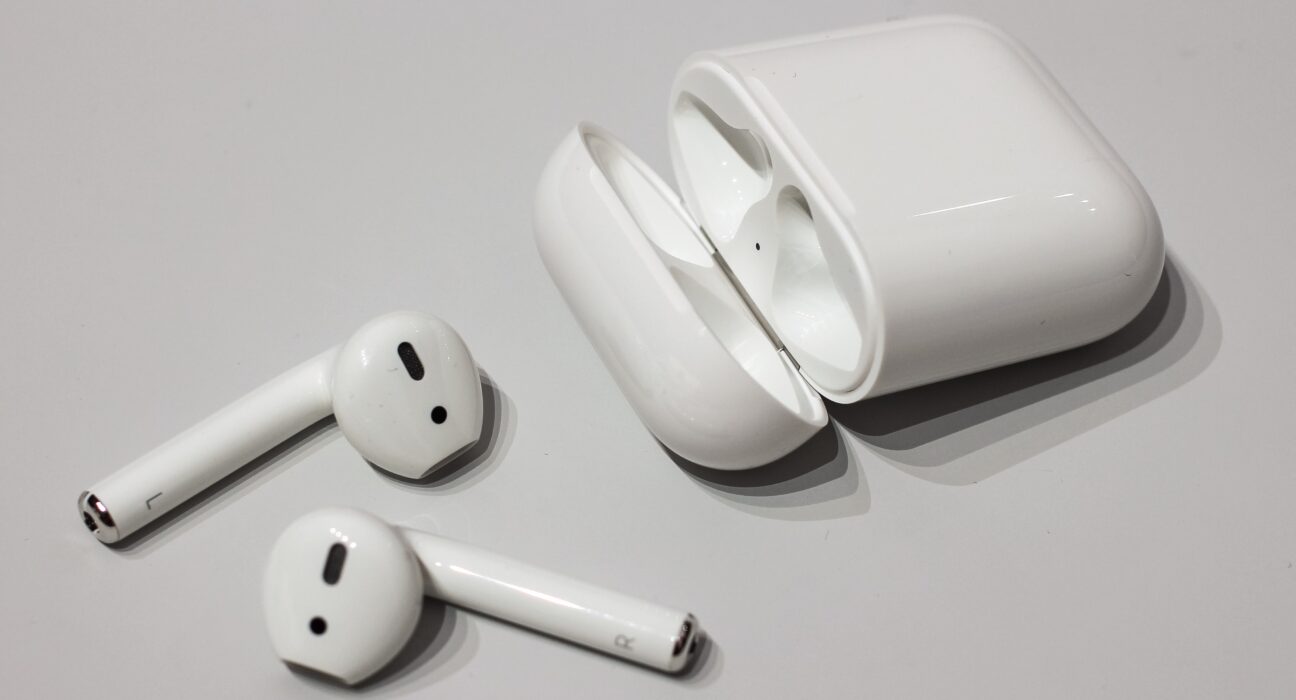Sepasang earbud nirkabel Apple AirPods berwarna putih dengan tangkai khas tergeletak di atas meja