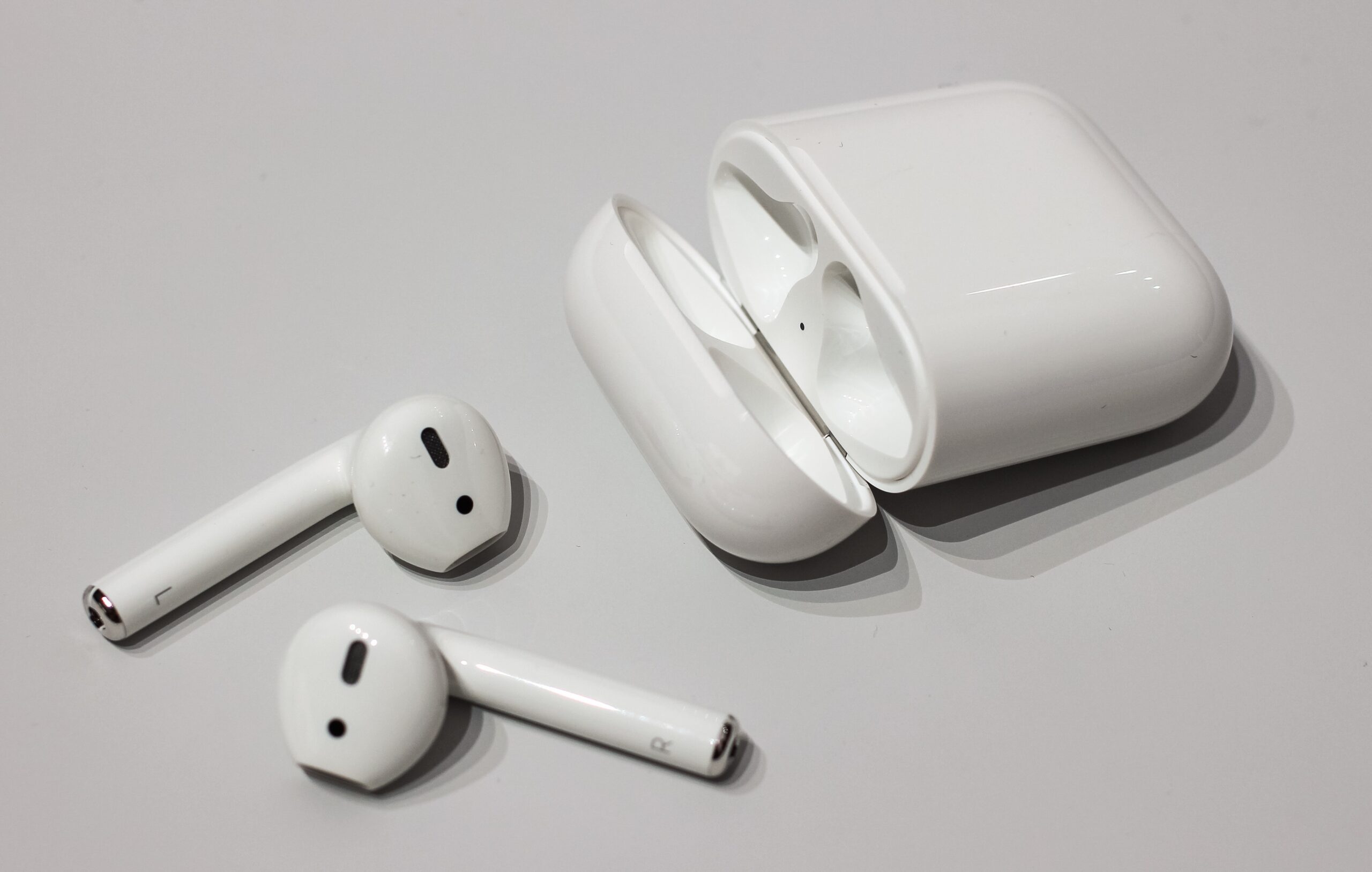 Sepasang earbud nirkabel Apple AirPods berwarna putih dengan tangkai khas tergeletak di atas meja